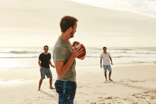 Man throwing football to one of two men on a Florida beach