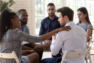 counselor leading group therapy session and offering support to someone sitting beside her