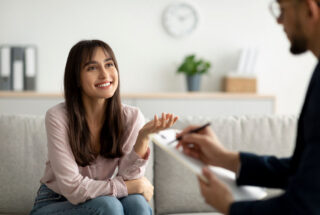 Smiling young woman talking with a counselor taking notes during a therapy session