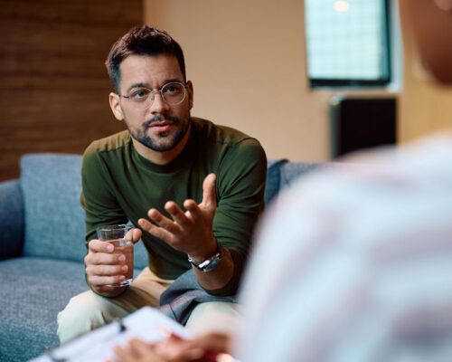Man holding a glass of water while talking with a counselor during a therapy session
