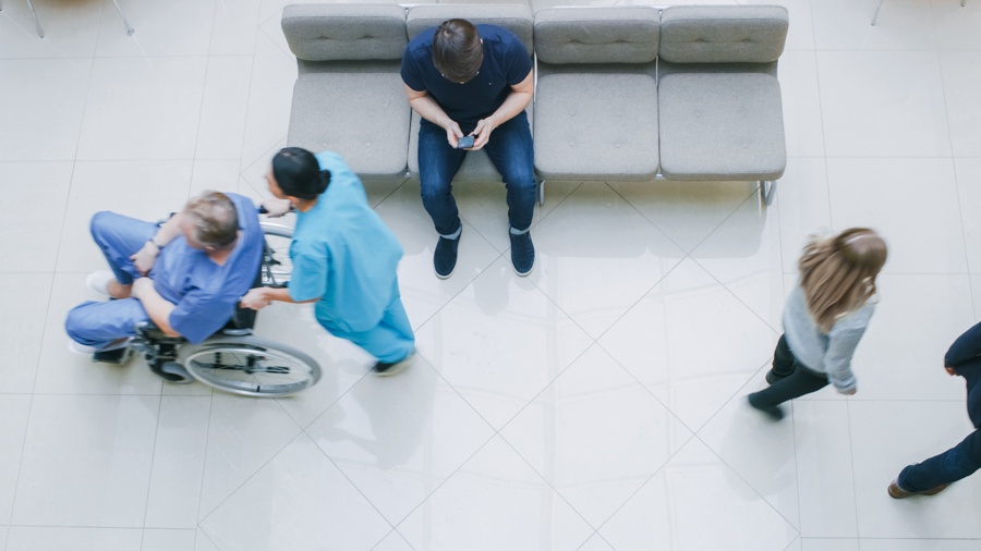 Man waiting in hospital with people walking through.
