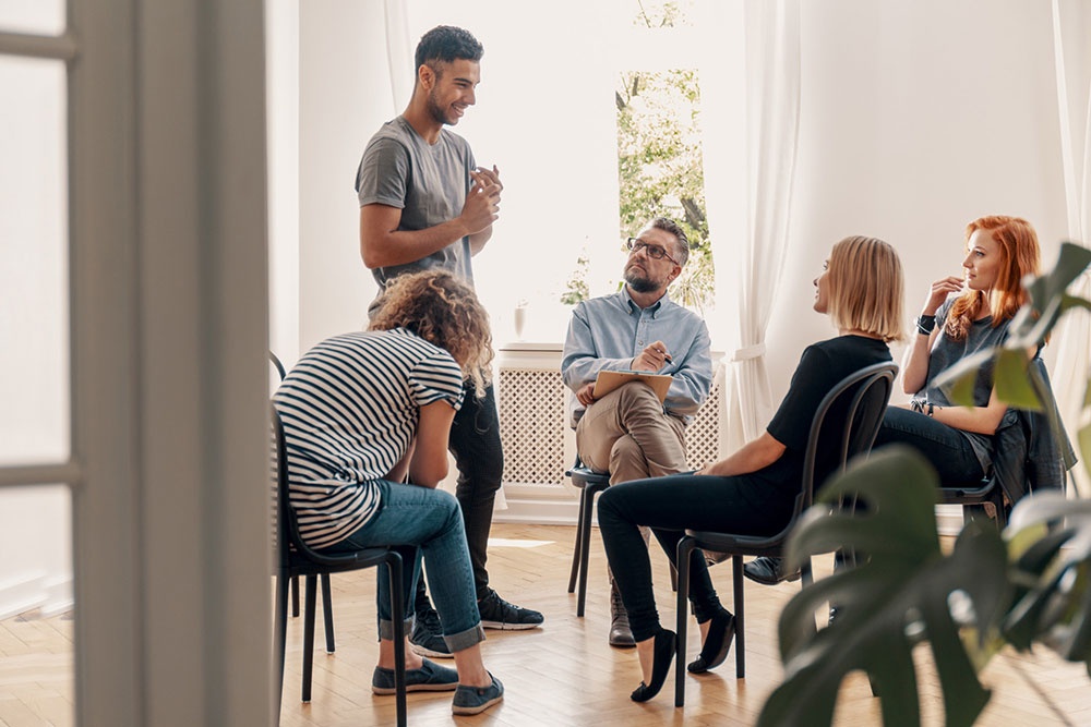 Man standing to speak during group therapy in stimulant addiction treatment.